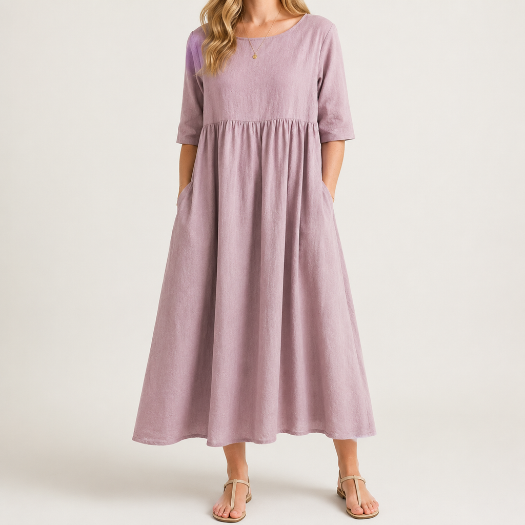 A woman wearing a dusty lavender midi dress with elbow-length sleeves, side pockets, and a gathered waist, paired with neutral sandals against a light beige studio background.
