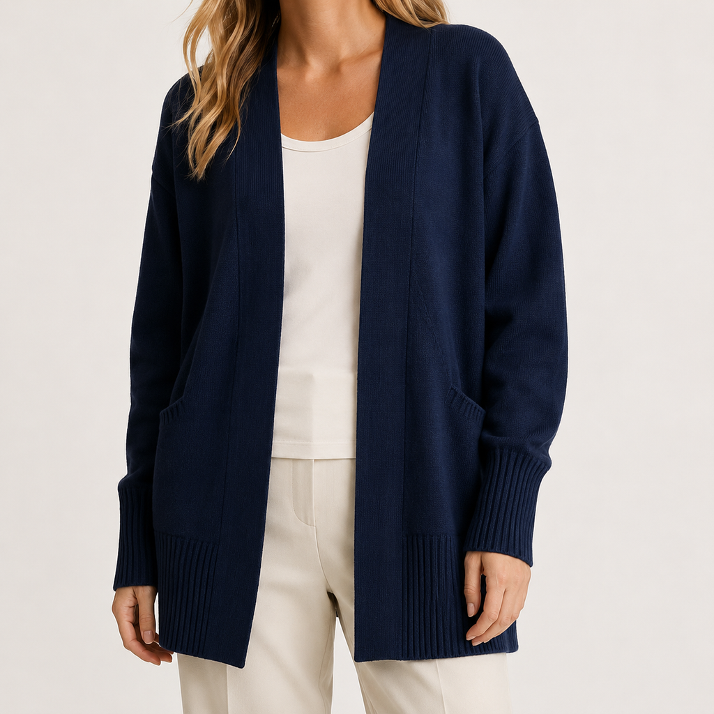 A woman wearing a navy blue open-front knit cardigan over a white top and cream pants, photographed against a clean light gray studio background.