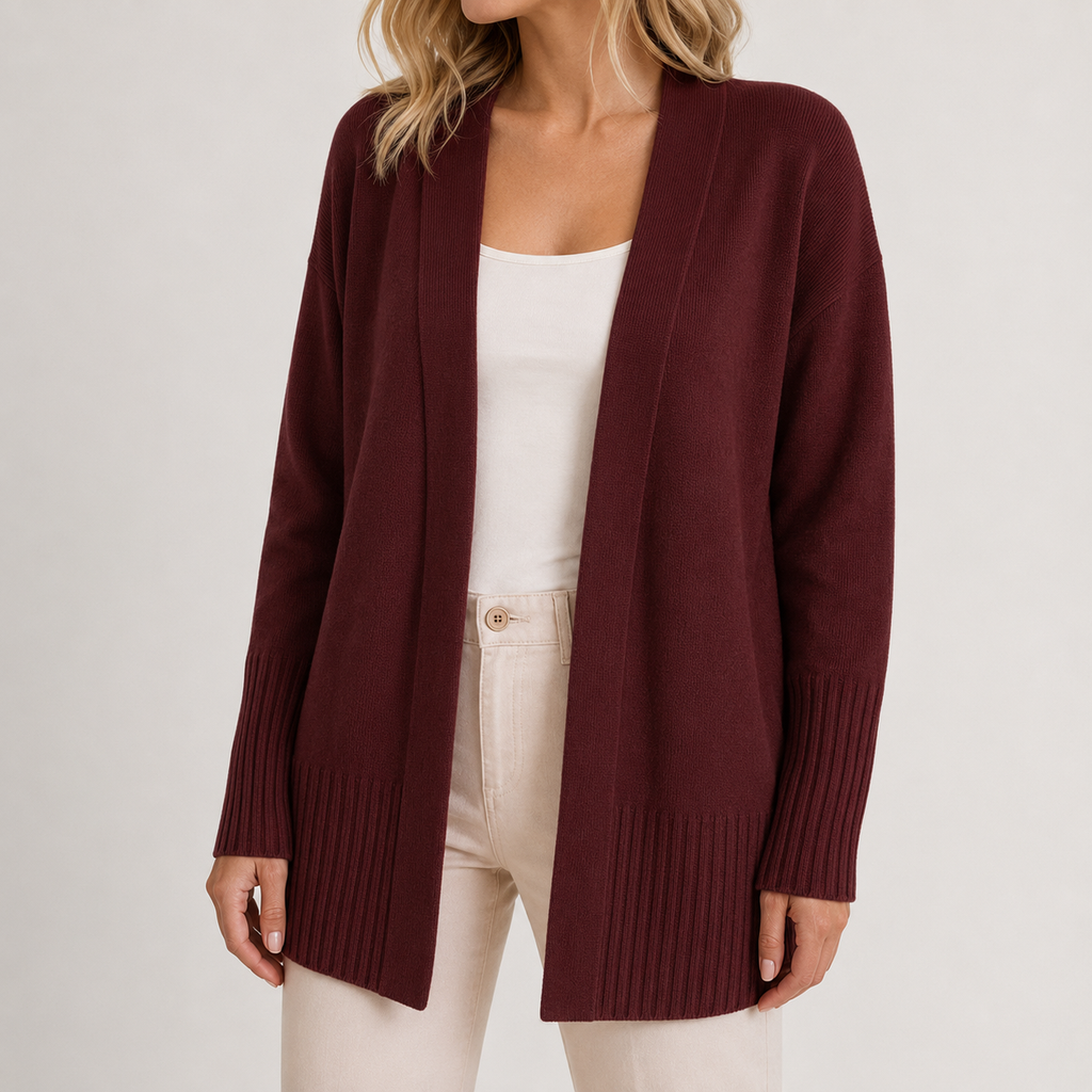 A woman wearing a burgundy open-front knit cardigan over a white tank top and cream pants, photographed against a clean light gray studio background.