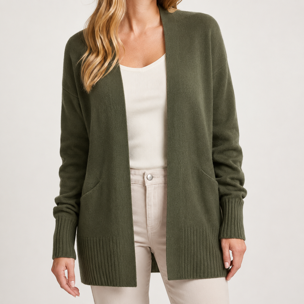 A woman wearing an olive green open-front knit cardigan over a white ribbed top and light beige pants, photographed against a plain light gray studio background.