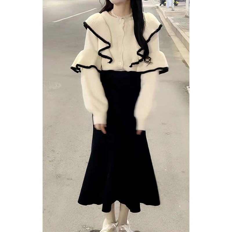 Cream knit sweater with black ruffled trim and button-down front, paired with a long black skirt.