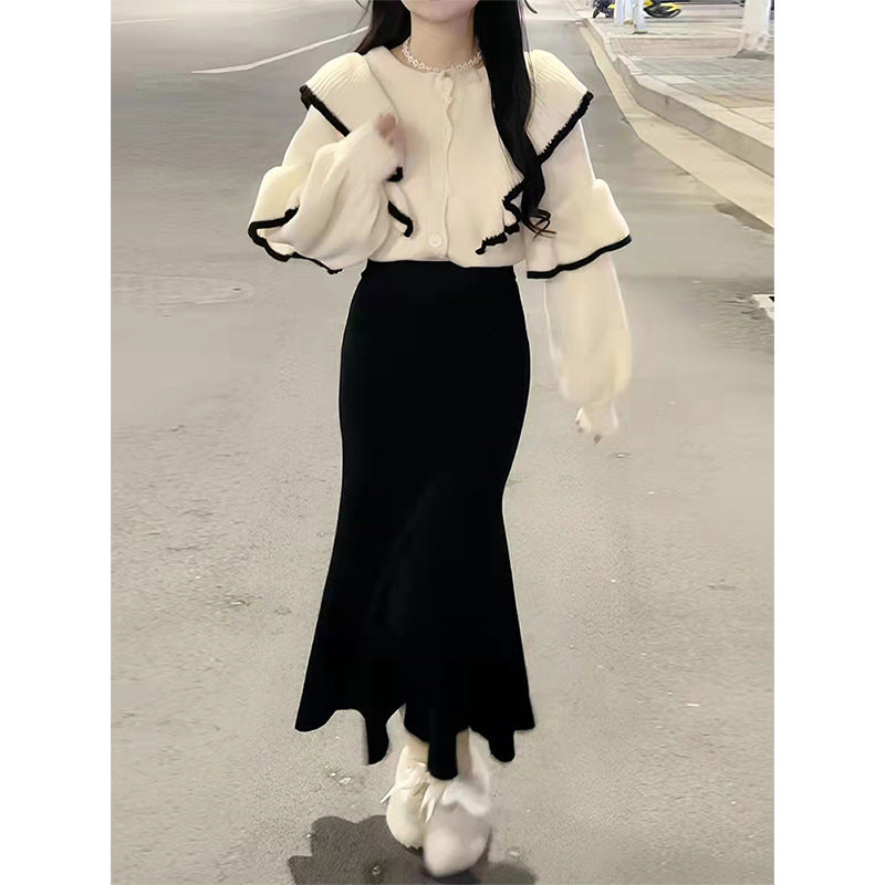 Cream knit sweater with black trim, ruffled collar, and long sleeves paired with a black midi skirt.