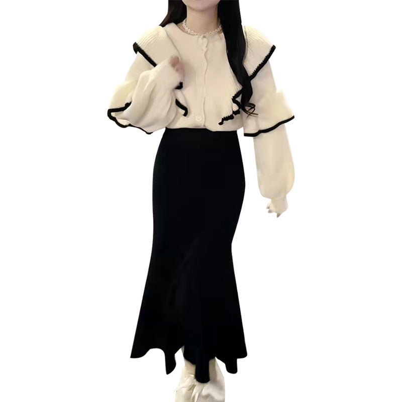 Cream knit sweater with black trim and ruffled collar paired with a black high-waisted midi skirt.