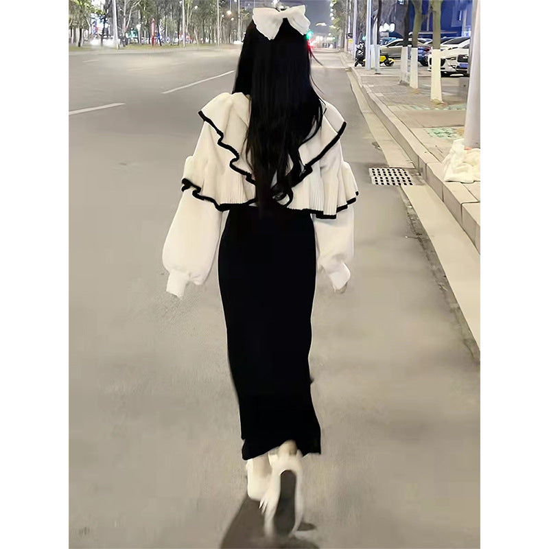 Woman wearing a white knit sweater with black ruffled trim, long sleeves, and a matching white hair bow, paired with a black skirt.