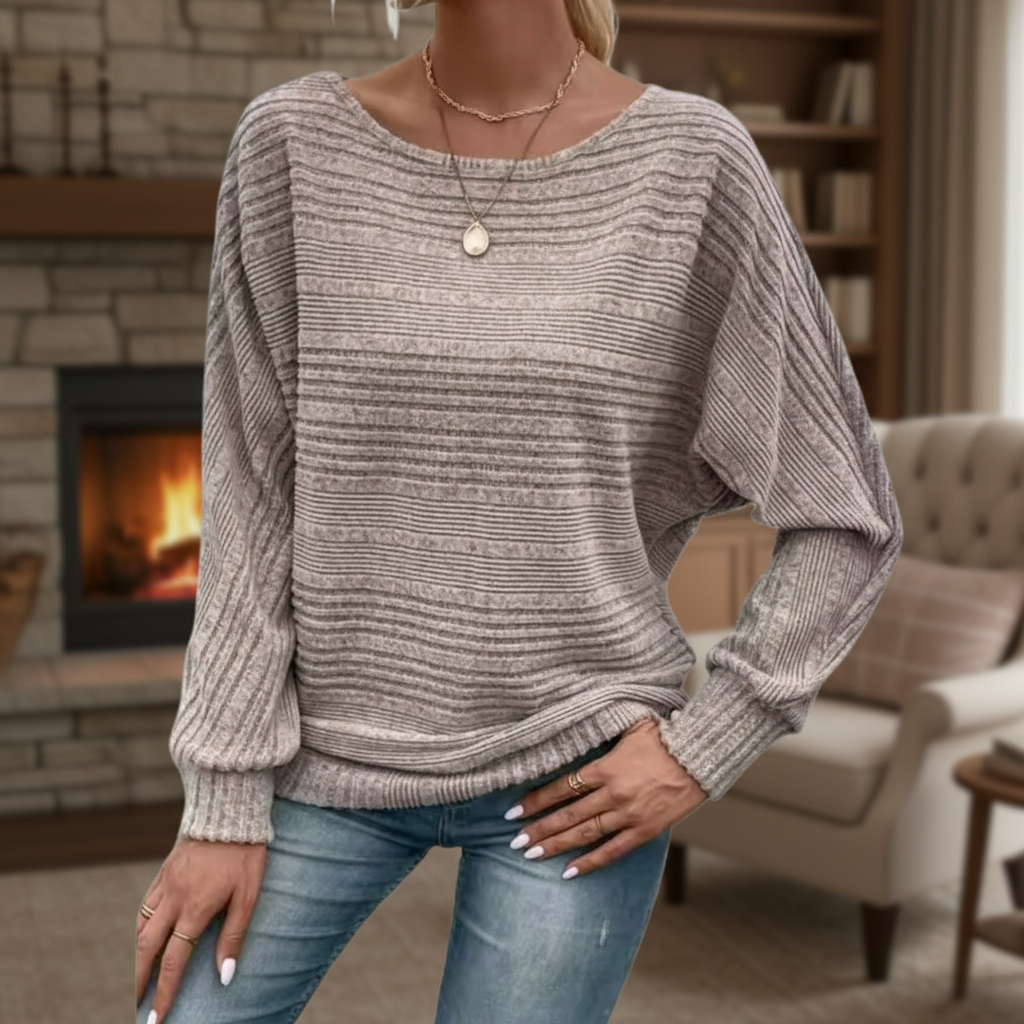 Taupe textured knit sweater with a wide round neckline, relaxed batwing sleeves, and ribbed cuffs paired with blue jeans.