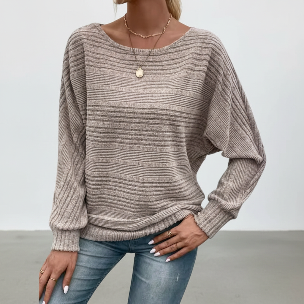 Taupe textured knit sweater with a wide round neck, batwing sleeves, and ribbed cuffs paired with blue jeans.