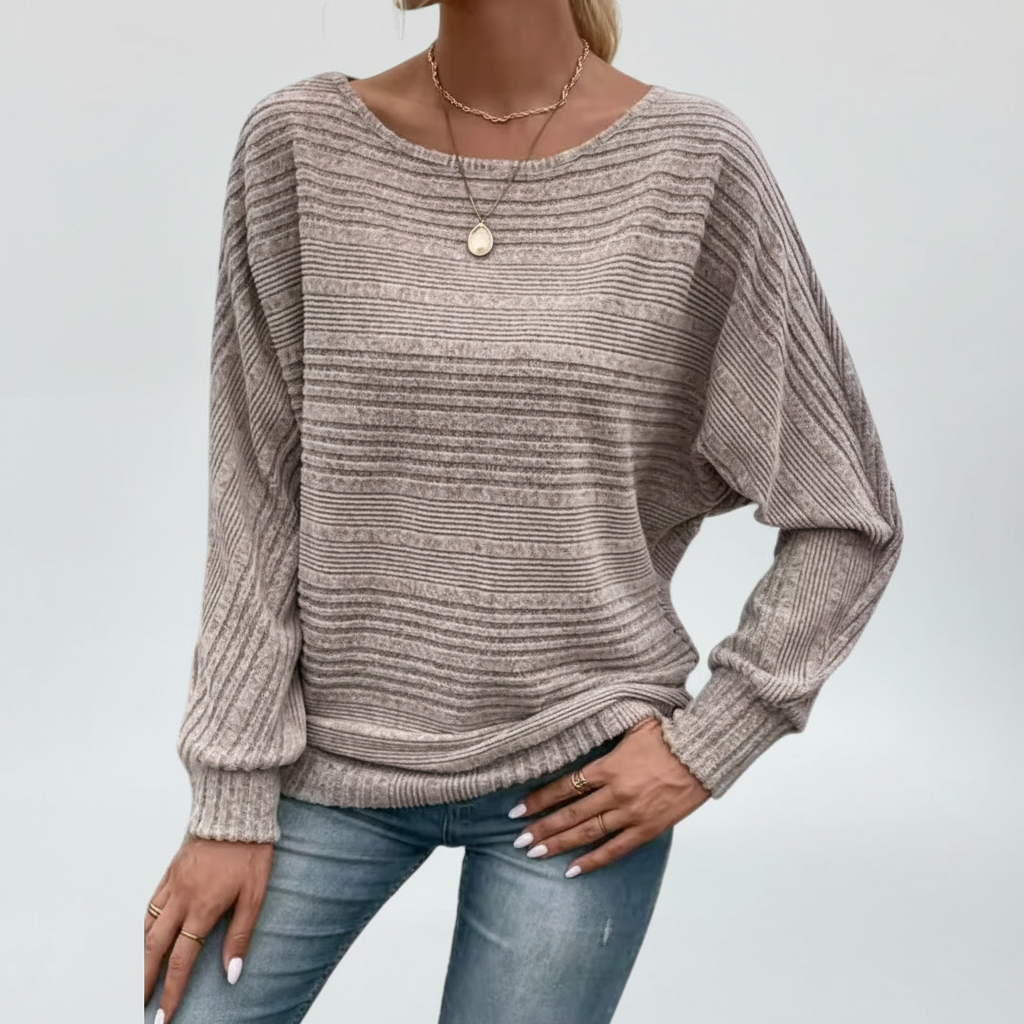 Taupe textured knit sweater with a wide round neckline, relaxed batwing sleeves, and ribbed cuffs paired with blue jeans.