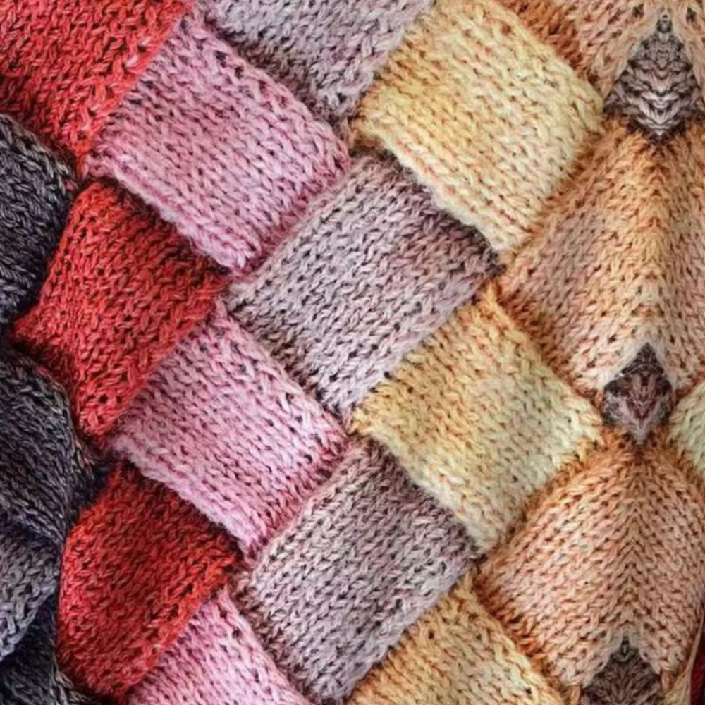 Close-up of a textured knit sweater featuring a vibrant, multi-colored woven square pattern in shades of red, pink, and yellow.