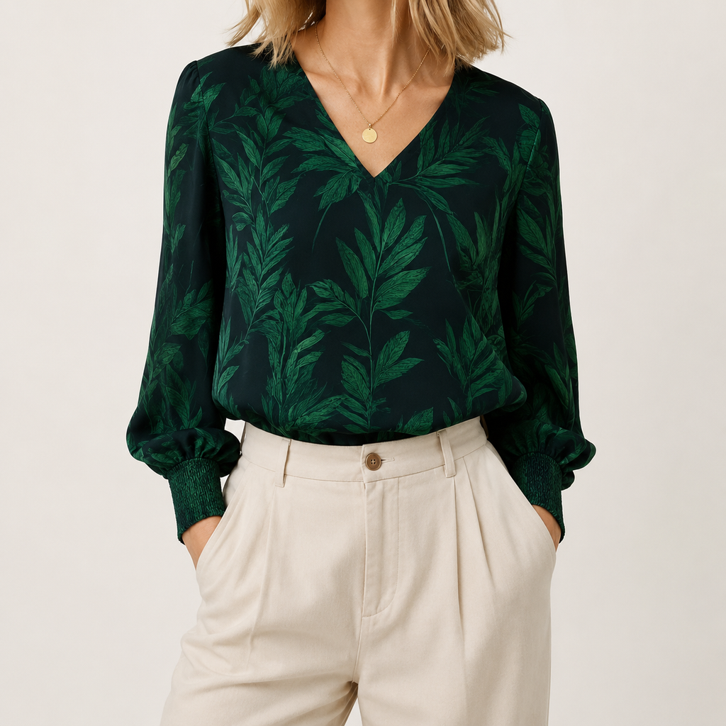 A woman wearing a dark green long-sleeve blouse with a lighter green tropical leaf pattern and cream-colored pleated trousers, photographed against a plain light background.