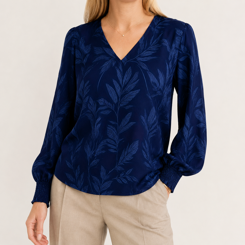 A woman wearing a navy blue long-sleeve blouse with a tonal leaf pattern and beige pants, photographed against a plain light background.