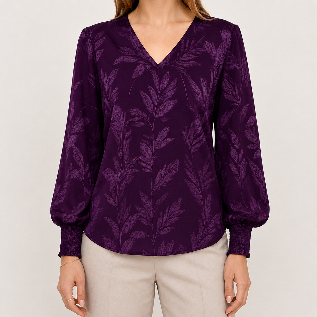 A woman wearing a long-sleeve V-neck blouse in deep purple with a tonal leaf pattern, paired with light beige pants, against a plain light gray background.