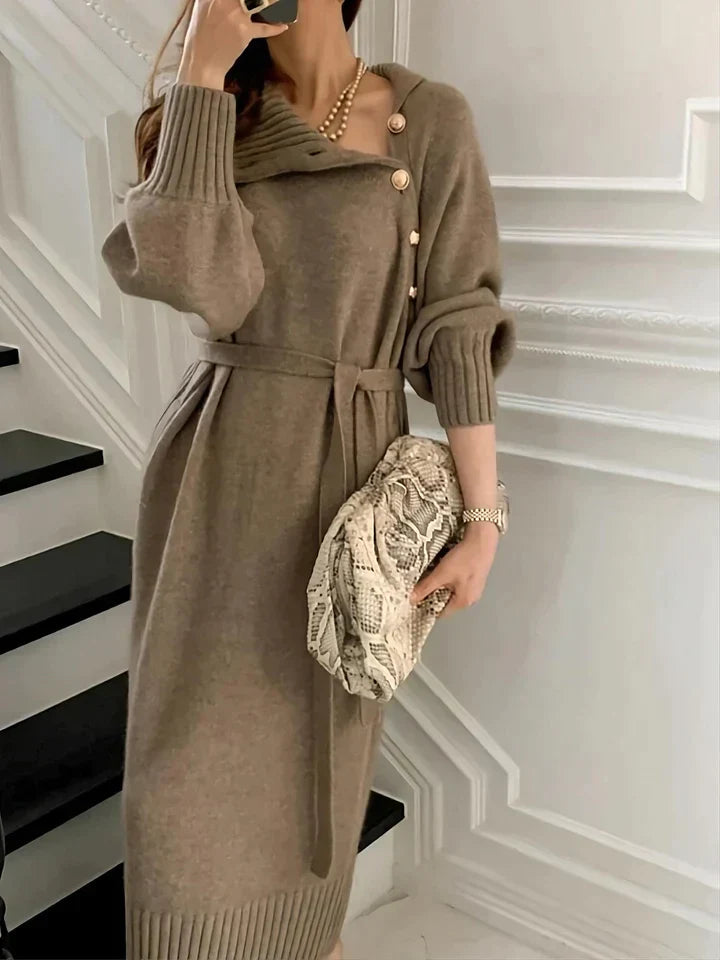 Taupe knit sweater dress with a buttoned turtleneck, tie waist, and ribbed cuffs, styled with a snakeskin clutch.
