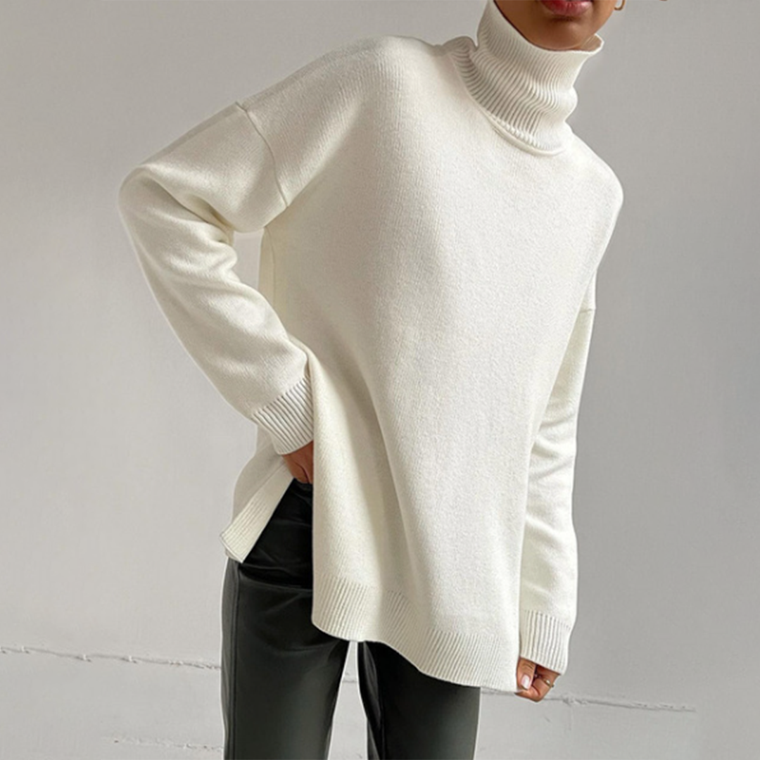 Off-white relaxed fit turtleneck sweater with a ribbed high neck and side split hem, worn with dark trousers.