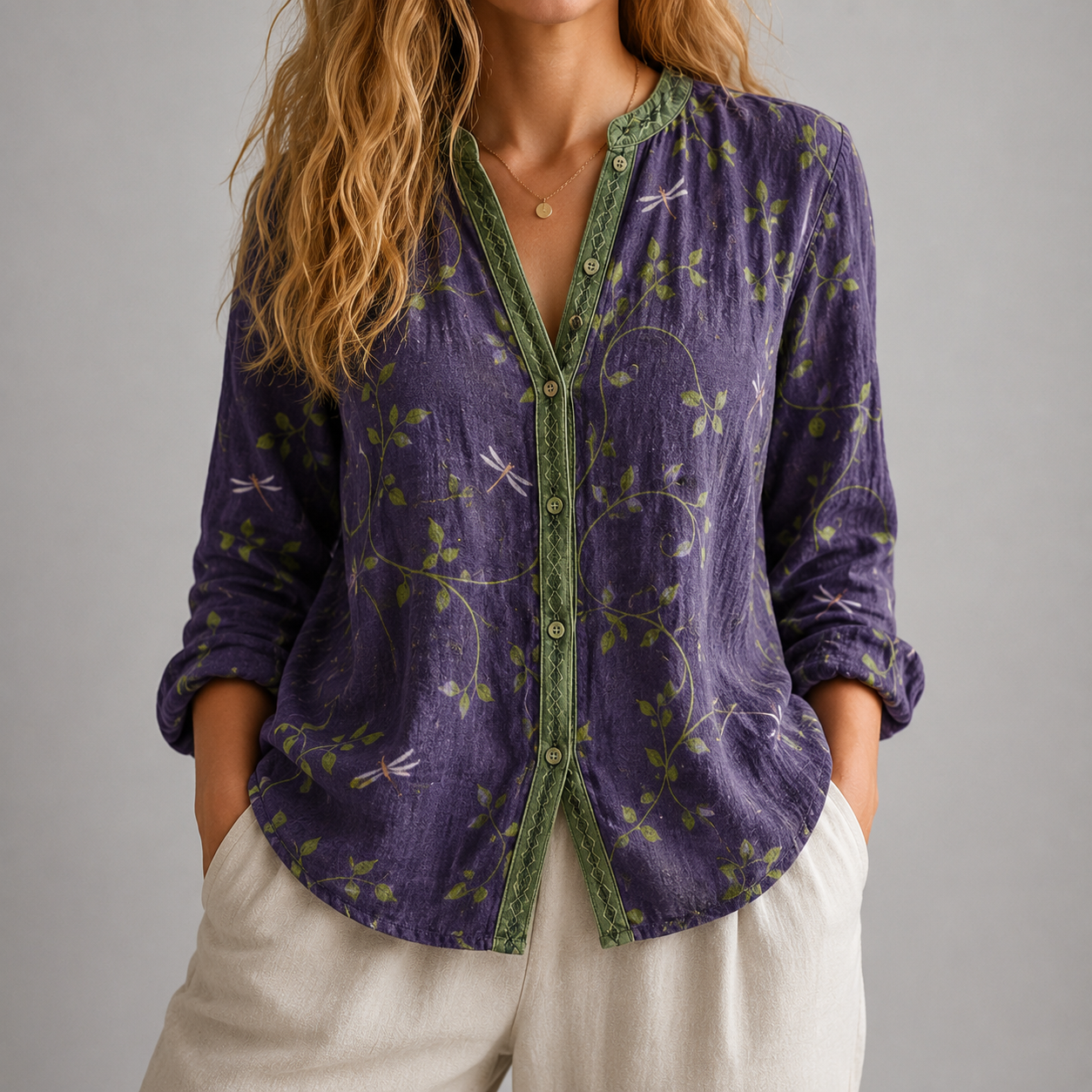 A woman wearing a purple long-sleeve button-up shirt with green leafy vine patterns and green trim, paired with off-white pants, against a neutral gray background.