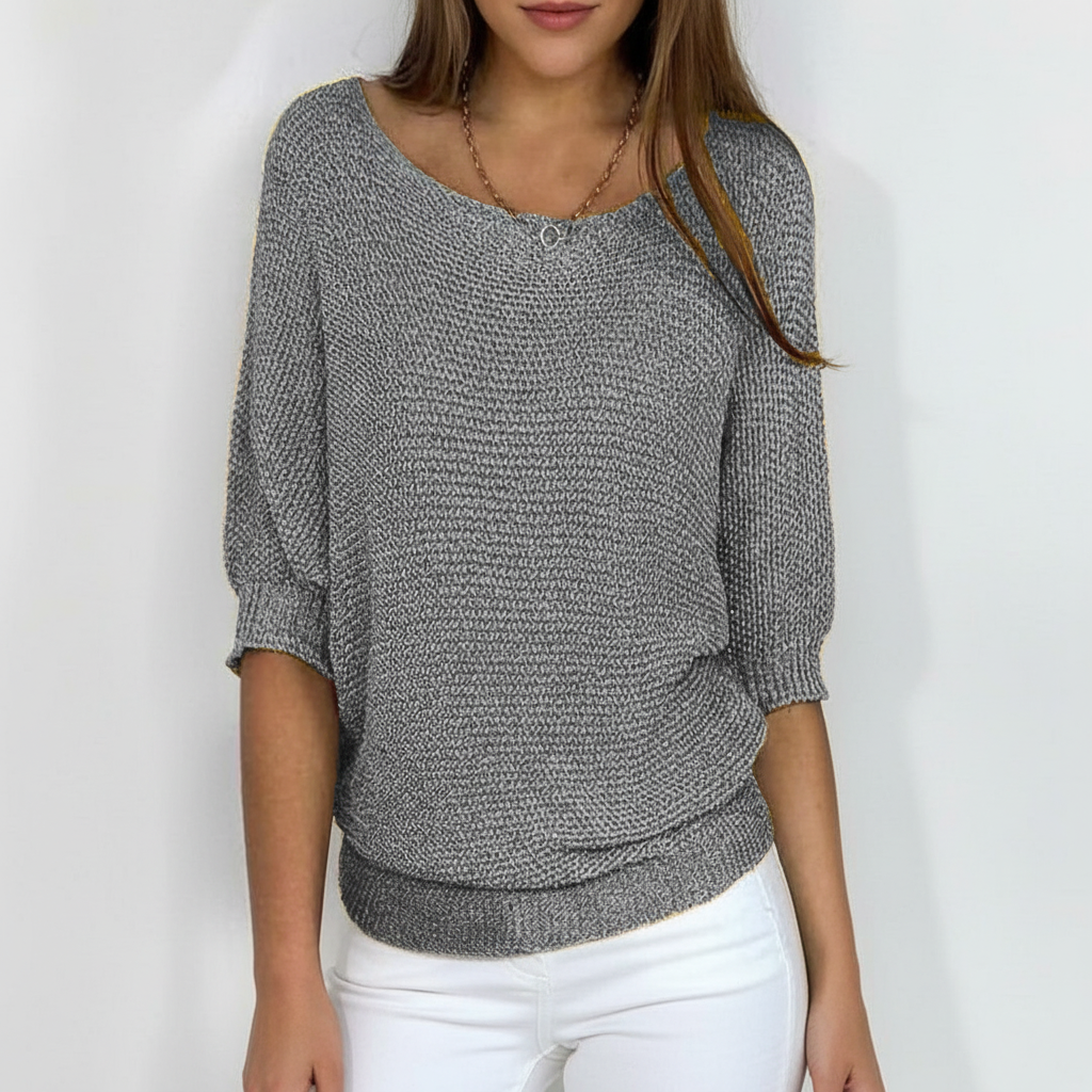 Grey relaxed-fit sweater with wide neckline, dolman sleeves, and ribbed cuffs paired with white pants.
