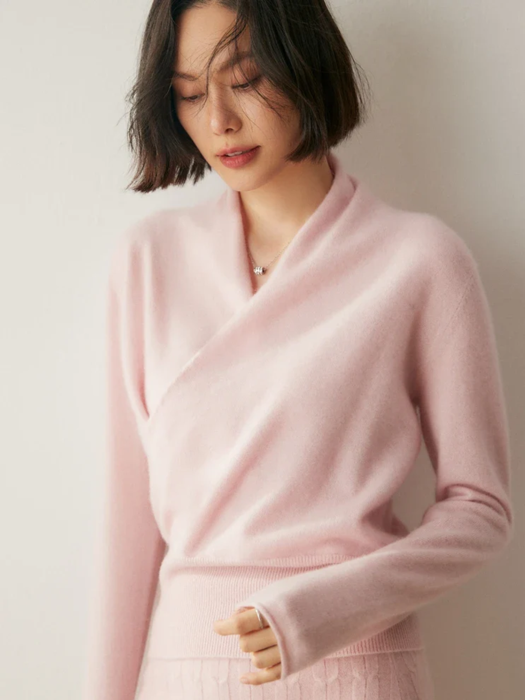 Slim-fit pink knit sweater featuring a feminine crossover wrap neckline and long sleeves with ribbed hem detailing.