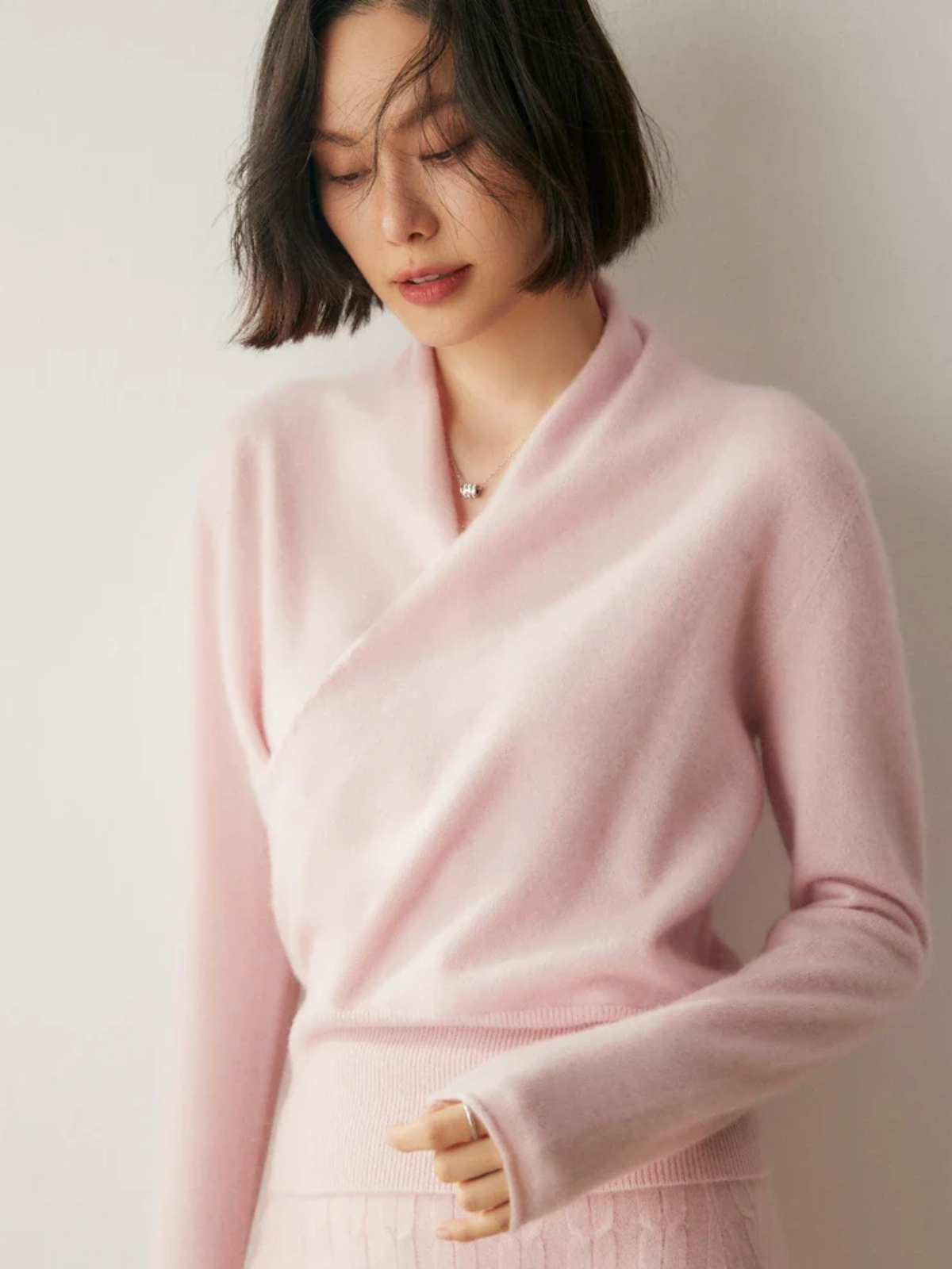 Slim-fit pink knit sweater featuring a feminine crossover wrap neckline and long sleeves with ribbed hem detailing.