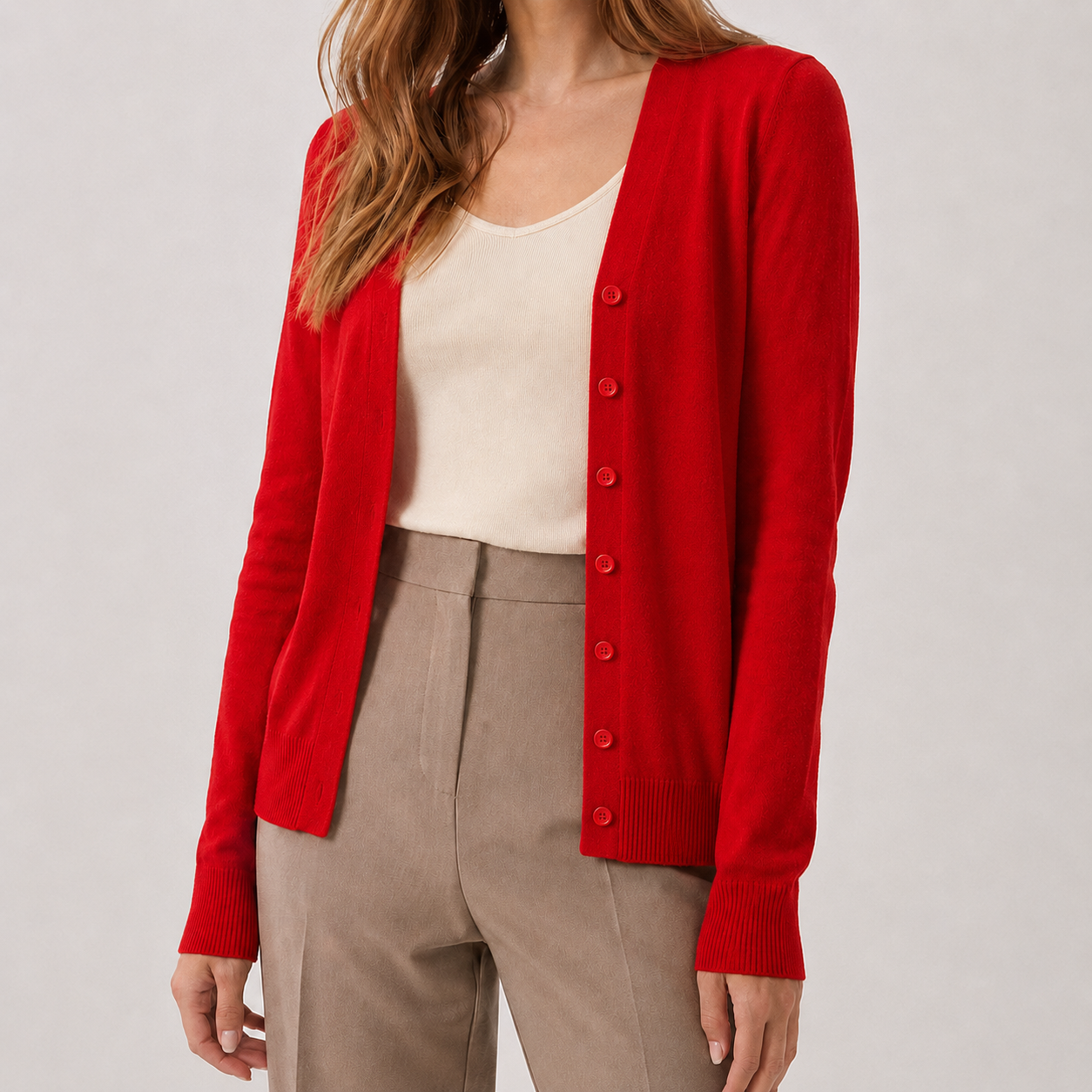 Bright red V-neck knit cardigan with a button-front, long sleeves, and ribbed cuffs worn over a cream top and trousers.